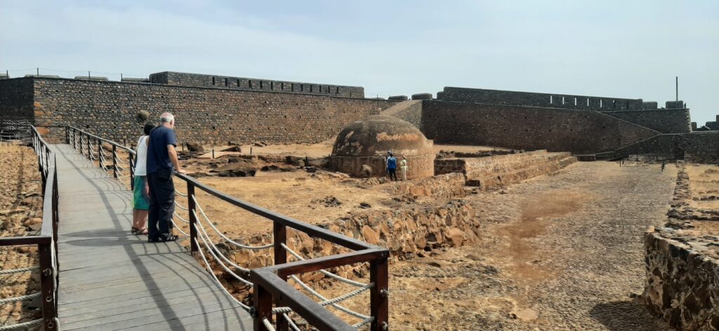 Ancient stone ruins and fortification walls at Forte Real de São Filipe, Cidade Velha, Cape Verde — wooden walkway leading into the site with visitors exploring the heritage landmark