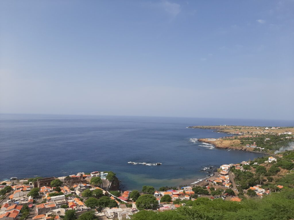 Coastal view of Cidade Velha, Cape Verde — red‑roofed houses and green vegetation overlooking a calm blue bay with rocky outcrops and a curved shoreline