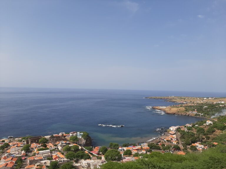 Coastal view of Cidade Velha, Cape Verde — red‑roofed houses and green vegetation overlooking a calm blue bay with rocky outcrops and a curved shoreline